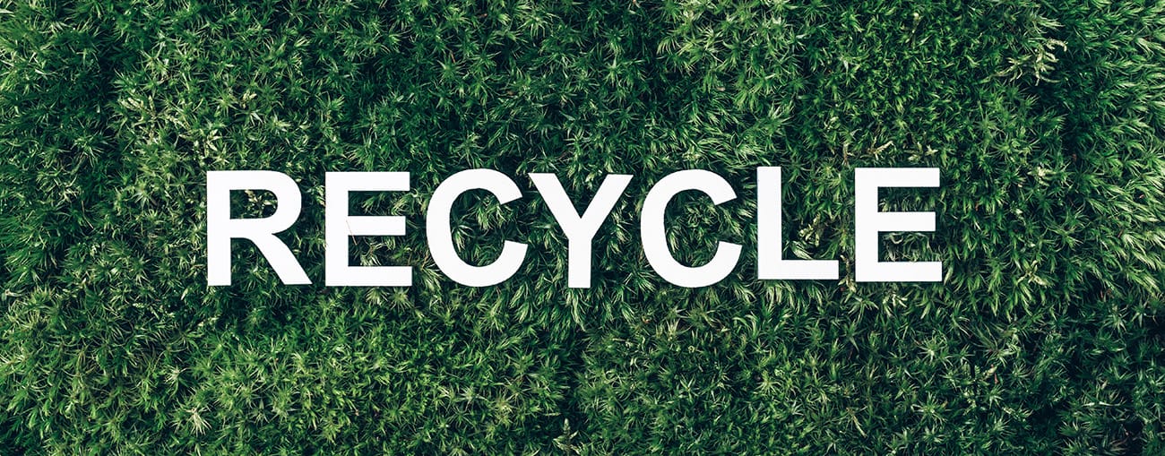 Het woord ‘Recycle’ op een groene achtergrond van mos, als symbool voor duurzame kleding en hergebruik van materialen.