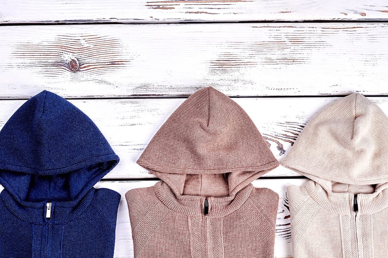 Duurzame hoodies in natuurlijke kleuren op een houten ondergrond, als voorbeeld van milieuvriendelijke fashion voor bedrijven.