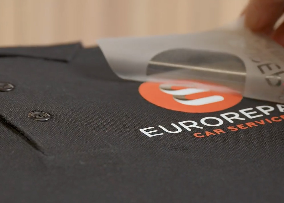 DTF bedrukking van een logo op bedrijfskleding met transferfolie tijdens het aanbrengen